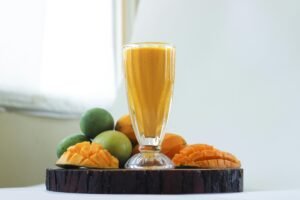 Delicious mango smoothie in a glass surrounded by fresh mangoes, perfect for a healthy refreshment.