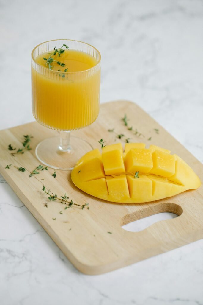 Delicious mango juice with fresh mango slices on a wooden board, garnished with herbs.